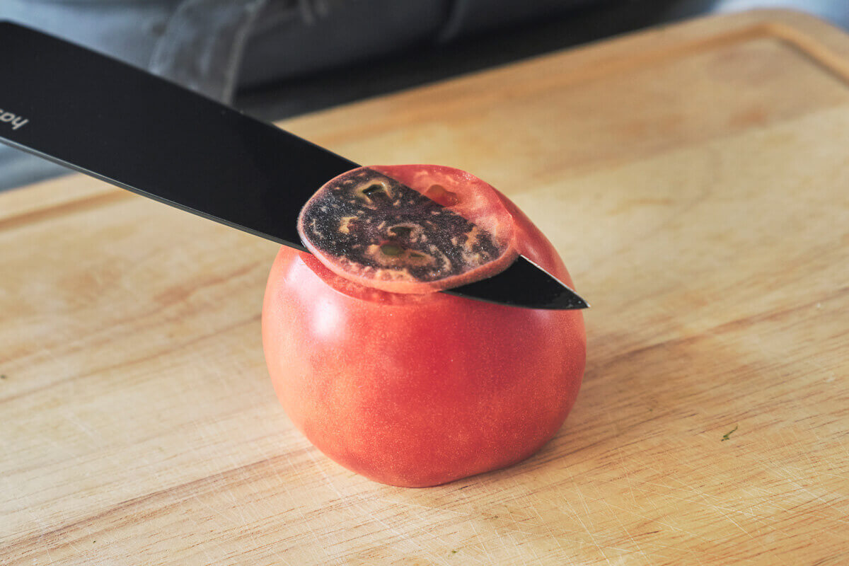 黒い包丁でトマトを切る